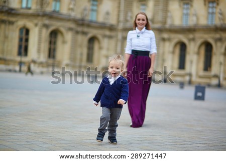 Beautiful young mother and her adorable toddler son having fun together in Palais Royal in Paris, boy is running from his mommy