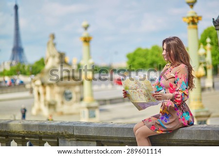 Beautiful young tourist with map of Paris in Tuileries garden on a sunny summer day