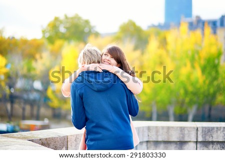 Young dating couple in Paris on a bright fall day, walking together by the Seine, colorful autumn leaves in the background