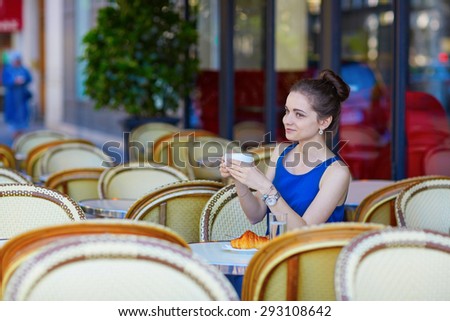 Beautiful young Parisian woman in blue blouse drinking coffee in an outdoor cafe on a summer day