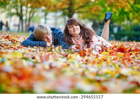 Young dating couple in Paris on a bright fall day sitting on the ground in autumn leaves