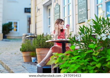 Beautiful young woman sitting in an outdoor cafe in Vienna, Austria and correcting her makeup