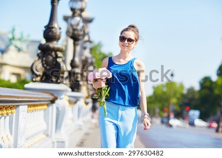 Beautiful young Parisian woman in blue tube top with bunch of pink peonies on the bank of the Seine