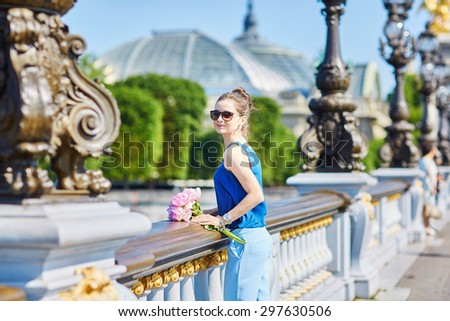 Beautiful young Parisian woman in blue tube top with bunch of pink peonies on the bank of the Seine