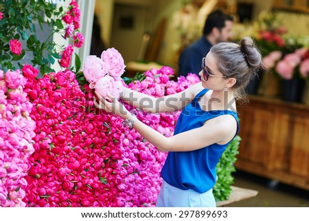 Beautiful young Parisian woman selecting pink peonies in French flower shop or at market