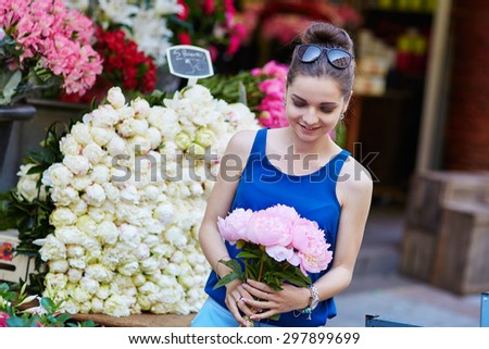 Beautiful young Parisian woman selecting pink peonies in French flower shop or at market