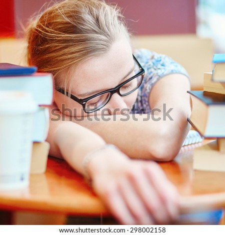 Beautiful young student with lots of books, sleeping on the table, tired of preparing for exams. Shallow DOF