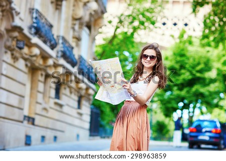 Beautiful young tourist in long skirt on a street of Paris near the Eiffel tower on a summer day, looking at the map and planning her itinerary