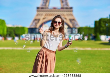 Beautiful young tourist or student girl in Paris blowing bubbles near the Eiffel tower on a summer day