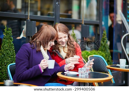 Two beautiful young girls drinking coffee and chatting in a Parisian street cafe on a fall or spring day