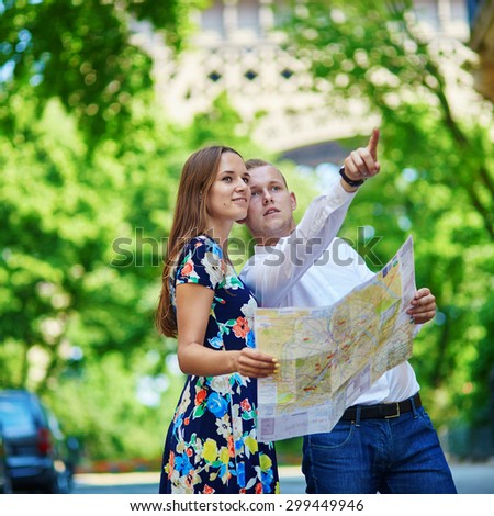 Couple of tourists using map and looking for the direction near the Eiffel tower in Paris