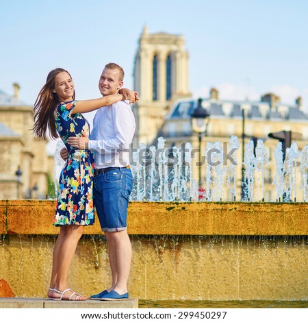 Romantic couple having fun together near the fountain on a hot summer day in Paris. Notre-Dame cathedral is in the background