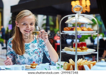 Beautiful young woman enjoying afternoon tea with selection of fancy cakes and sandwiches in a luxury Parisian restaurant