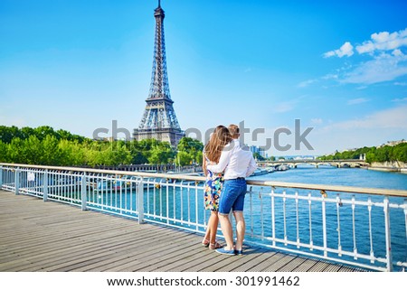 Young romantic couple having a date and looking at the Eiffel tower on a bridge over the Seine in Paris, France