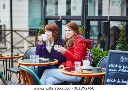 Two cheerful girls drinking coffee and chatting in a Parisian street cafe