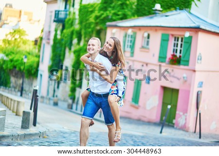 Young romantic couple having a date on a street of Montmartre near a pink house in Paris, France, man is piggybacking his girlfriend