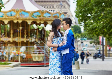 Young romantic Asian couple having a date near the traditional French merry-go-round, Eiffel tower is in the background, Paris, France