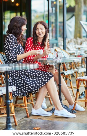 Beautiful twin sisters drinking coffee in a cozy outdoor cafe in Paris, France. Happy smiling girls enjoy their vacation in Europe