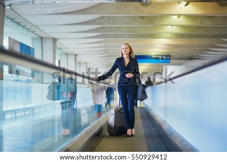 Young elegant woman with hand luggage on travelator on international airport terminal. Cabin crew member with suitcase. Travel or business trip concept