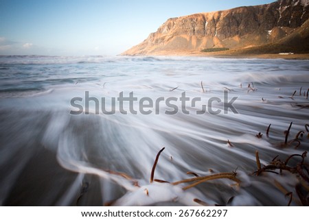 Long exposure showing wave movement around rocks and seaweed on Unstad beach, Lofoten, Norway