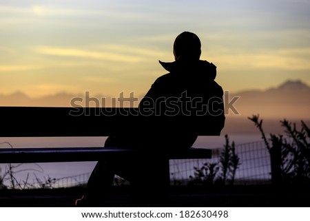 Silhouette of man on bench watching sunset