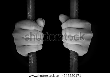 Man sits in captivity. Keeps hands behind bars