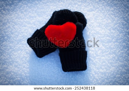 The little heart is lying on the snow on mittens. On the nature