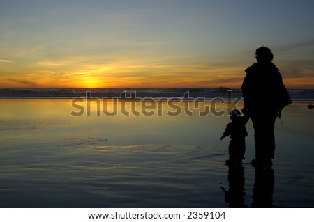Daughter and mother watch sunset hand in hand at Pacific ocean beach in San Francisco.