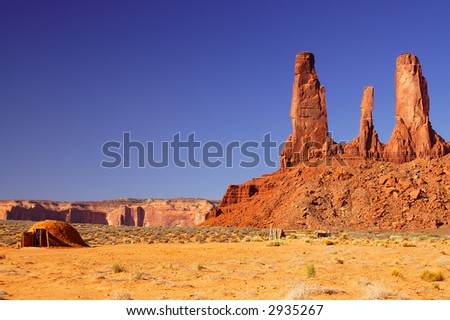 Three Sisters mesa in Monument Valley and traditional indian dwelling with tourist looking inside.