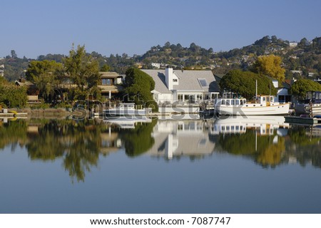 Nice houses with boats are reflected in calm waters of Corte Madera Creek in Larkspur, California.
