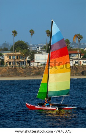 Athletic woman adjusts rigging on her yacht in Mission Bay, San Diego, California with a parasail in the background.