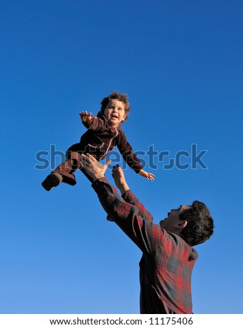 A happy two year old girl tossed into the blue sky by her father.