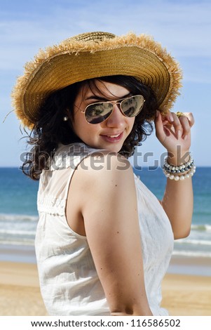 Close view detail of a beautiful young woman with a straw hat in summer clothes, smiling with the sea as a background.