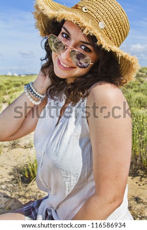 Close view detail of a beautiful young woman with a straw hat in summer clothes, smiling on a  beautiful landscape with typical dune vegetation.