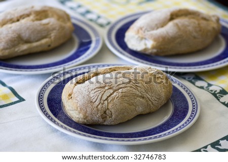 View of three fresh, baked loafs of small breads inside of three plates on top of a table.