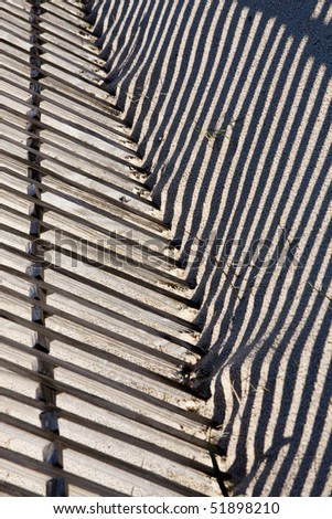 View of a section of a fence buried on the sand making a shadow.