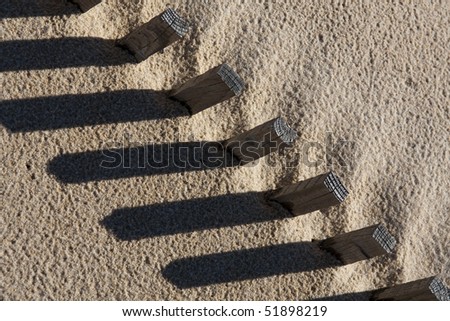 View of a section of a fence buried on the sand making a shadow.