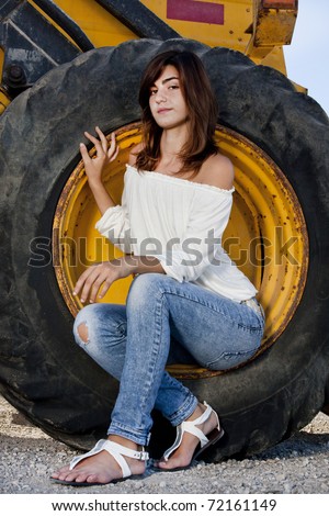 View of a beautiful girl sitting on a wheel of construction machine.