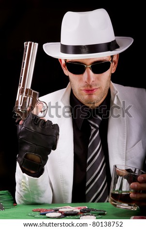 View of a gangster man playing some cards and poker, holding a gun.