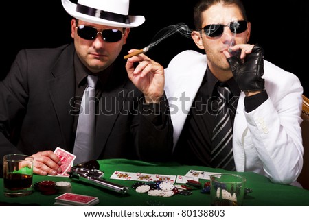 View of two gangster males playing some poker and smoking Cuban cigars.
