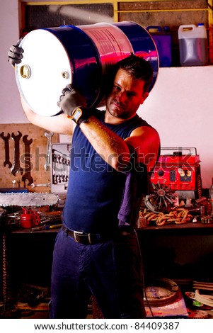 View of a happy garage mechanic man holding an oil barrel.
