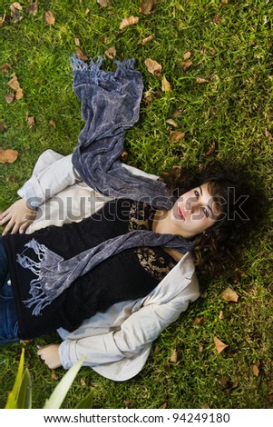 Beautiful young girl lies down on the green grass with fallen leaves.