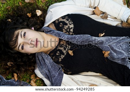 Beautiful young girl lies down on the green grass with fallen leaves.