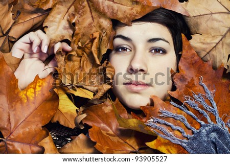 Close view of the face of a beautiful girl surrounded by autumn leaves.