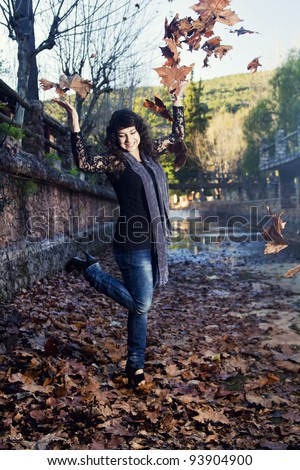 Beautiful girl throws in the air a bunch of autumn leaves.