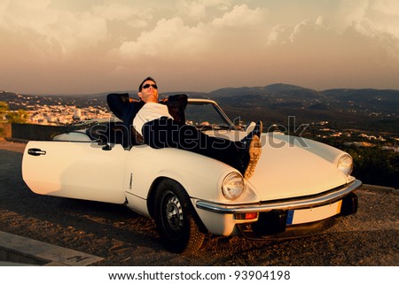 View of a young male with a jacket next to his white convertible car.