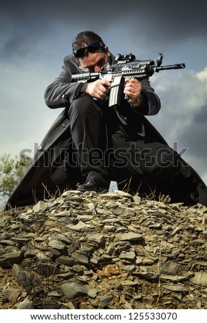 View of a contracted type killer agent wandering with a long jacket and machine gun.