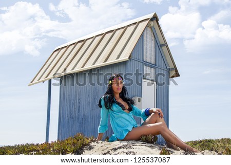 View of a beautiful woman in bikini in the beach, bathed by the sunny rays of Summer next to a blue wood house.