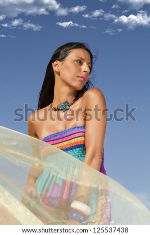 View of a beautiful woman in a colorful dress in the beach, bathed by the sunny rays of Summer.