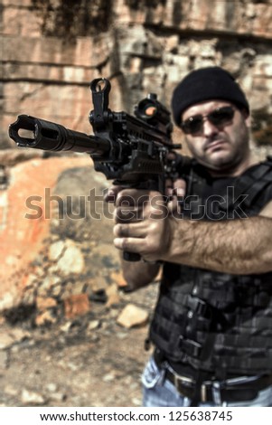 View of a man with a machine gun in jeans and jacket on a stone quarry.